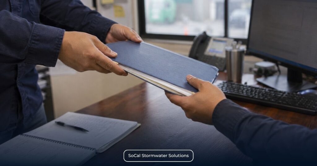 Industrial facility staff handing prepared stormwater reporting documents to an authorized reviewer for final SMARTS Annual Report certification.